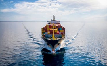 Aerial front view of a loaded container cargo vessel traveling over calm ocean