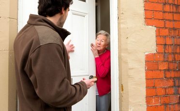 A horizontal image of a male door salesman putting an older lady under pressure to buy.