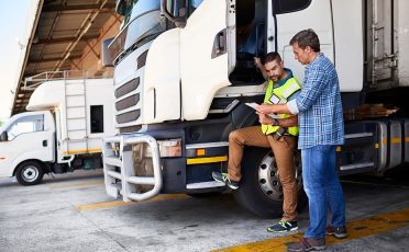 Shot of two coworkers talking together next to a large truck outside of a distribution center